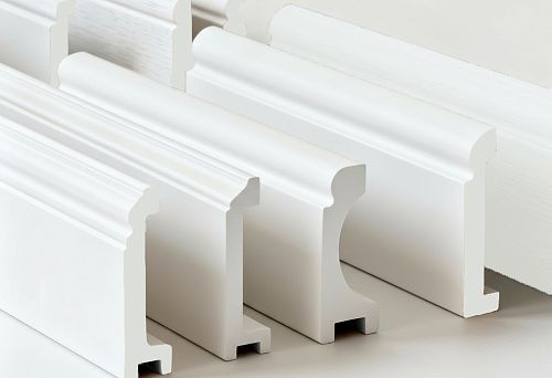 White skirting boards and cornices of various profiles, made from polystyrene and duropolymer, shown in close-up for comparing shape and material.