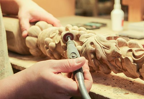 Craftsman processes a carved wooden element using electric tools, giving the item clear shapes and smoothness