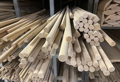 Round-section wooden poles of various diameters, neatly arranged on shelves in a production room
