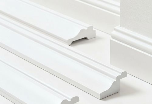 Белые плинтусы из дюрополимера и полистирола с фигурным профилем, представленные на светлом фоне для визуального сравнения форм и материалов.