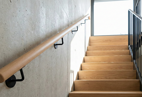 Round handrail made of light beech, mounted on black metal brackets on a concrete wall