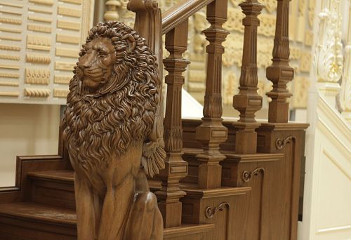 Decorative carved support post in the shape of a lion at the base of a wooden staircase