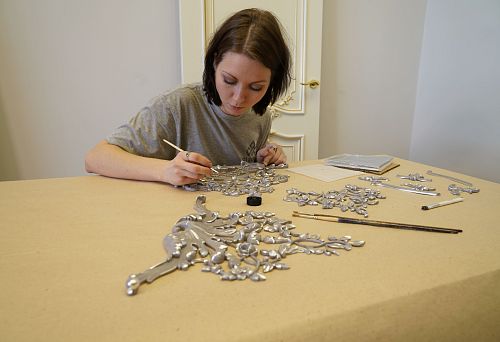 Girl manually paints a decorative carved element with silver paint