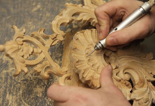 Process of manual restoration of carved wooden element: the master restores details of classical ornament using a graver