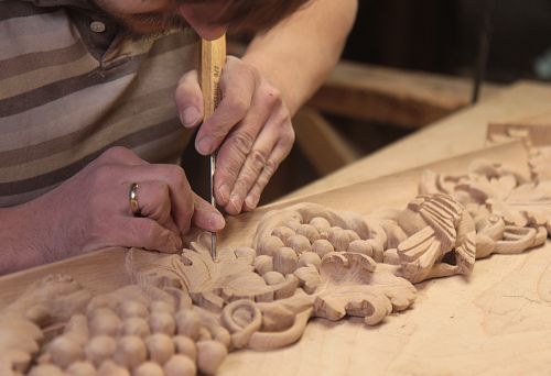 The craftsman manually carves a decorative wooden element with grapevine &mdash; the process of creating architectural framing