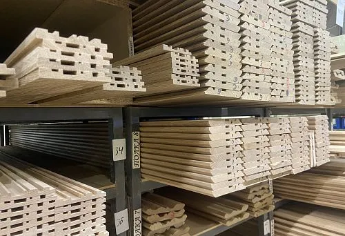 Carved wooden rods and profile blanks from solid wood, neatly arranged on shelves in the production workshop