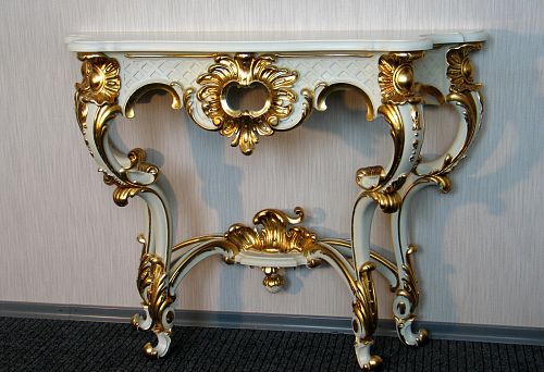 Luxurious console table base with hand-carved details and gold ornamentation in classic style against a light wall