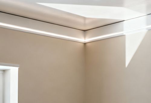 Плинтус под натяжной потолок с интегрированной LED-подсветкой, установленный по периметру потолка в современном интерьере с мягкими световыми акцентами.