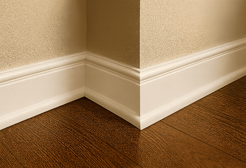 White large baseboard at the junction of wooden floor and wall in interior