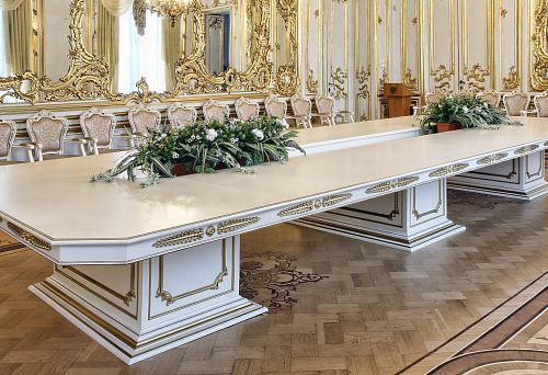 Elegant large wooden table with carving and gilding in a luxurious hall.