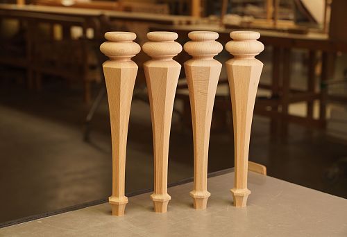 Four precisely crafted furniture legs made of solid natural wood on a workbench.