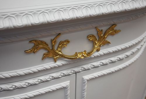 Gilded decorative furniture handle in the form of an elegant plant ornament on a white carved facade