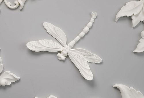 Decorative polyurethane ceiling molding: relief dragonfly, floral ornaments, elegant leaves and flowers on a light gray background.