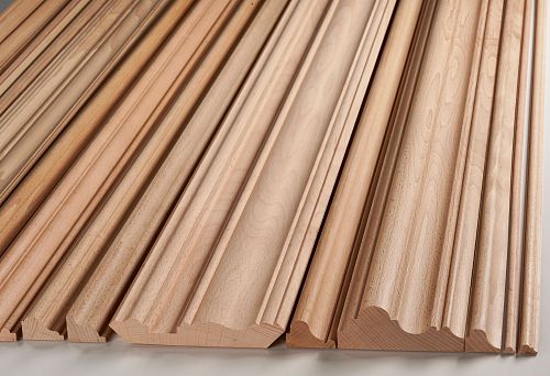 A row of long wooden elements with different profiles, arranged in a row on a light background.