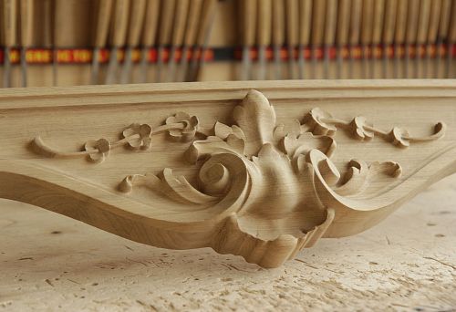 Carved decorative oak element with smooth scrolls and floral ornament against the backdrop of a workshop.